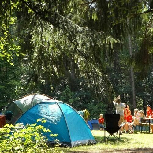 Zu sehen sind auf einer Zeltwiese zwei Zelte sowie Gäste, die auf einer Bank sitzen.